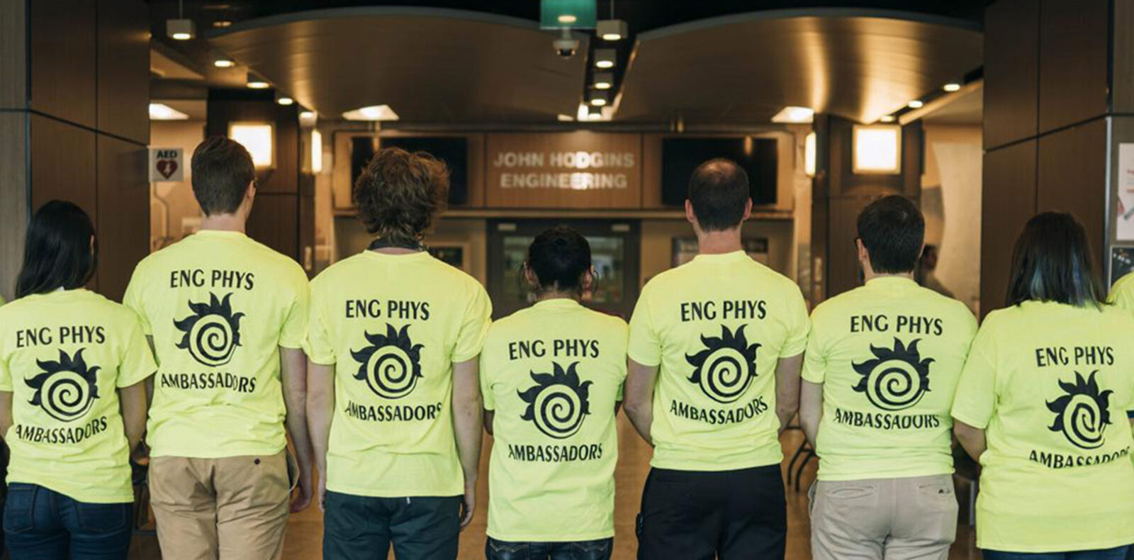 Students stand in a line with their back to the camera. Their shirts say "engineering physics ambassadors."