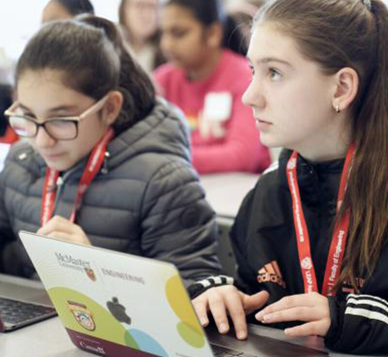 Two girls code on their laptops.