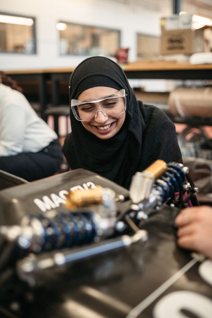 Javayria Mudassar wears safety goggles and smiles as she bends forward over some machinery.