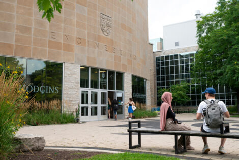 Students sit on a bench outside the John Hodgins Engineering Building entrance