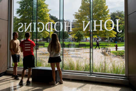 Three students look out the window of the John Hodgins Engineering lobby