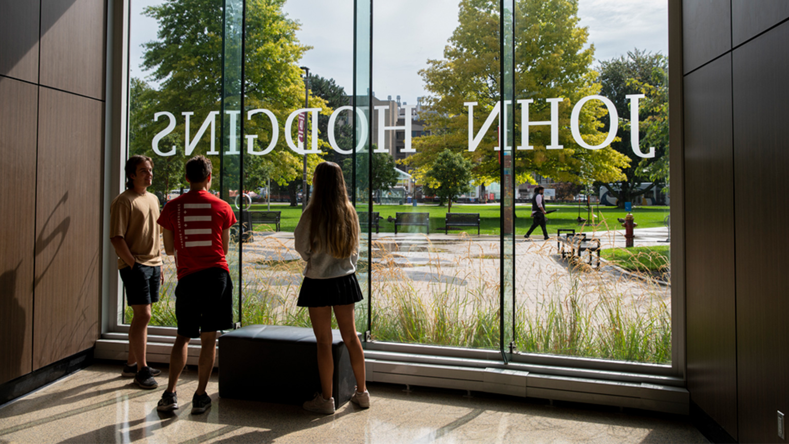 Three students look out the window of the John Hodgins Engineering lobby