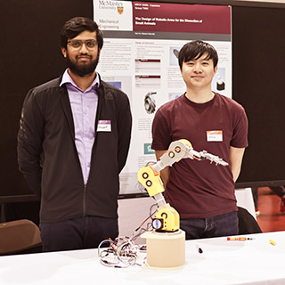 Two students standing with a robotic arm