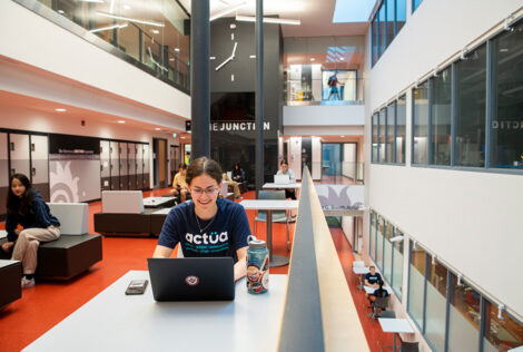 A student smiles while working on a laptop in the junction, a part of the Hatch Centre.