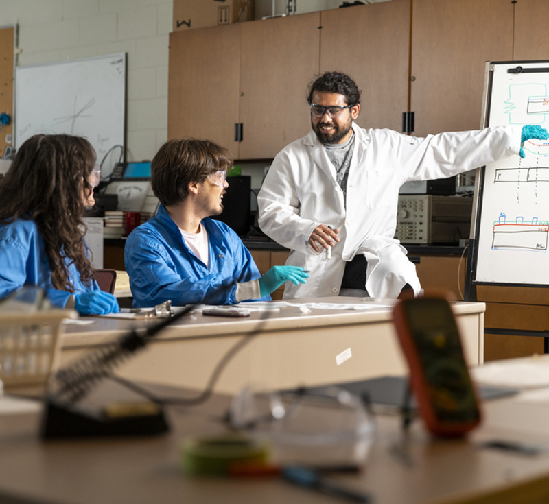 Instructor with two students in a lab, explaining a concept on a whiteboard