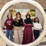 Four women students standing in front of the iron ring on campus.