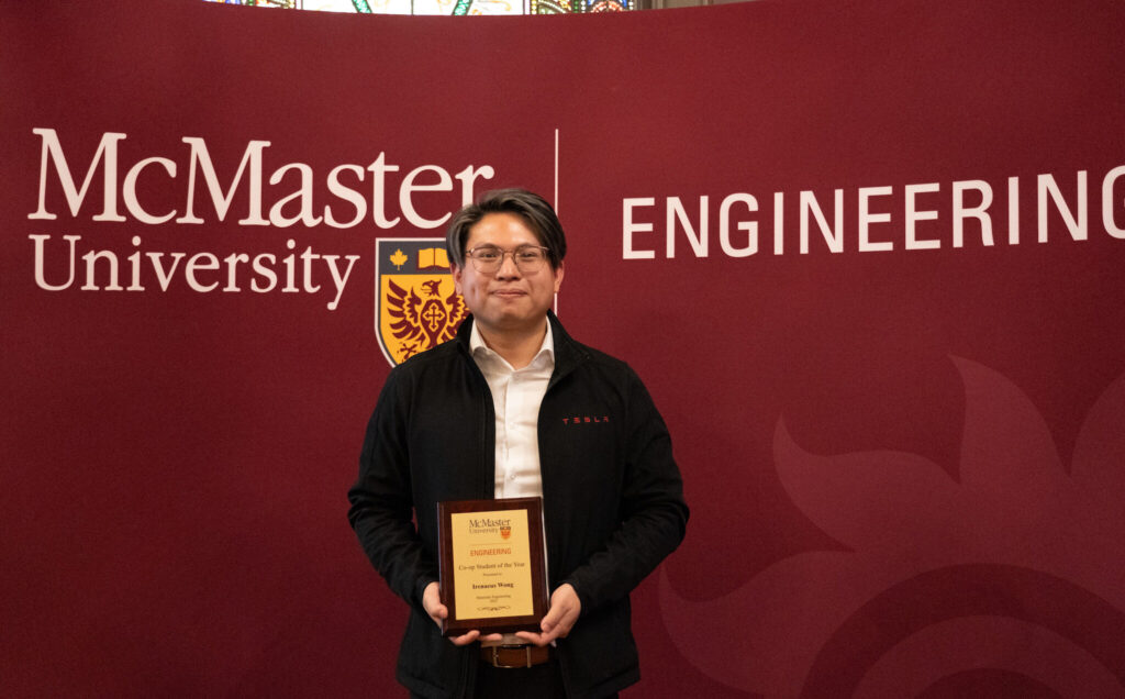 person standing in front of a McMaster University sign holding an award. 