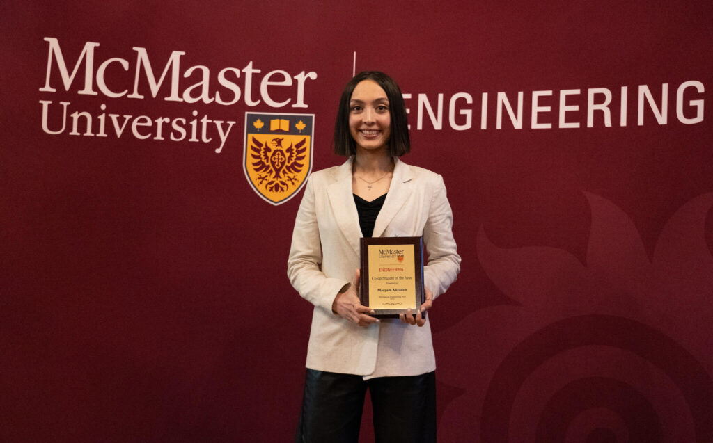 person standing in front of a McMaster University sign holding an award. 