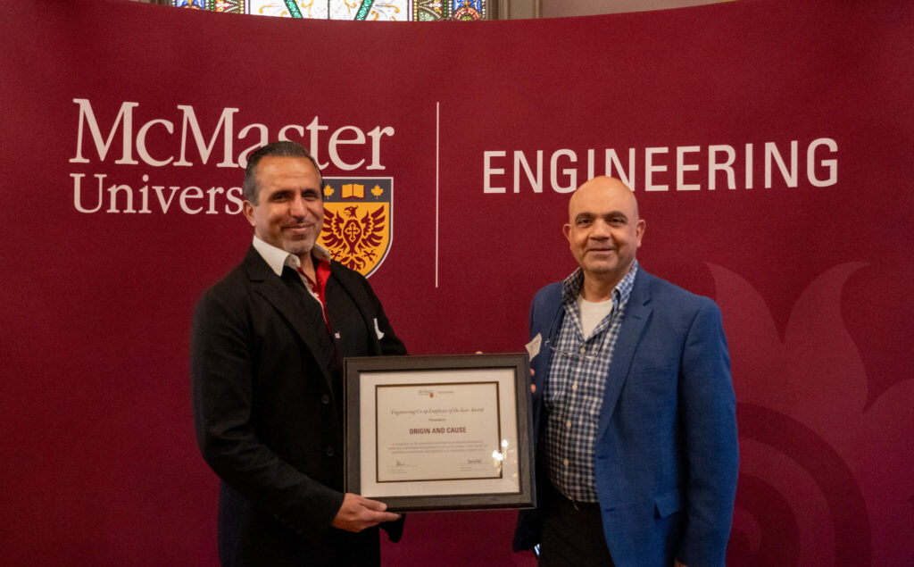two men standing in front of a McMaster University sign holding an award.