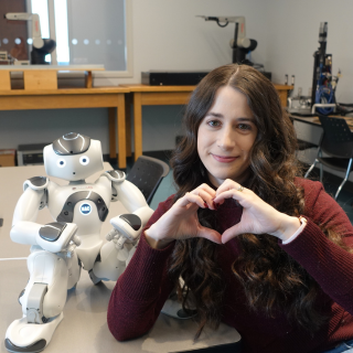 Denise Geiskkovitch poses with heart hands next to a robot