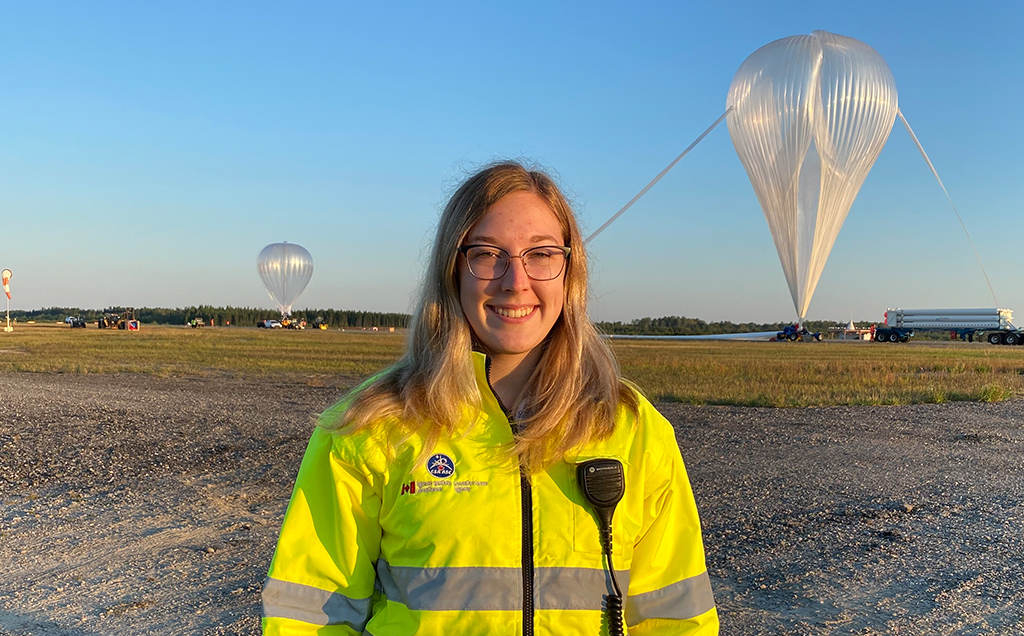 Magalie wears a bright yellow CSA jacket with stratospheric balloons in the background