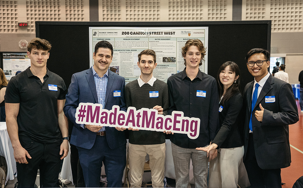 A capstone group poses with the #MadeAtMacEng sign in front of their poster