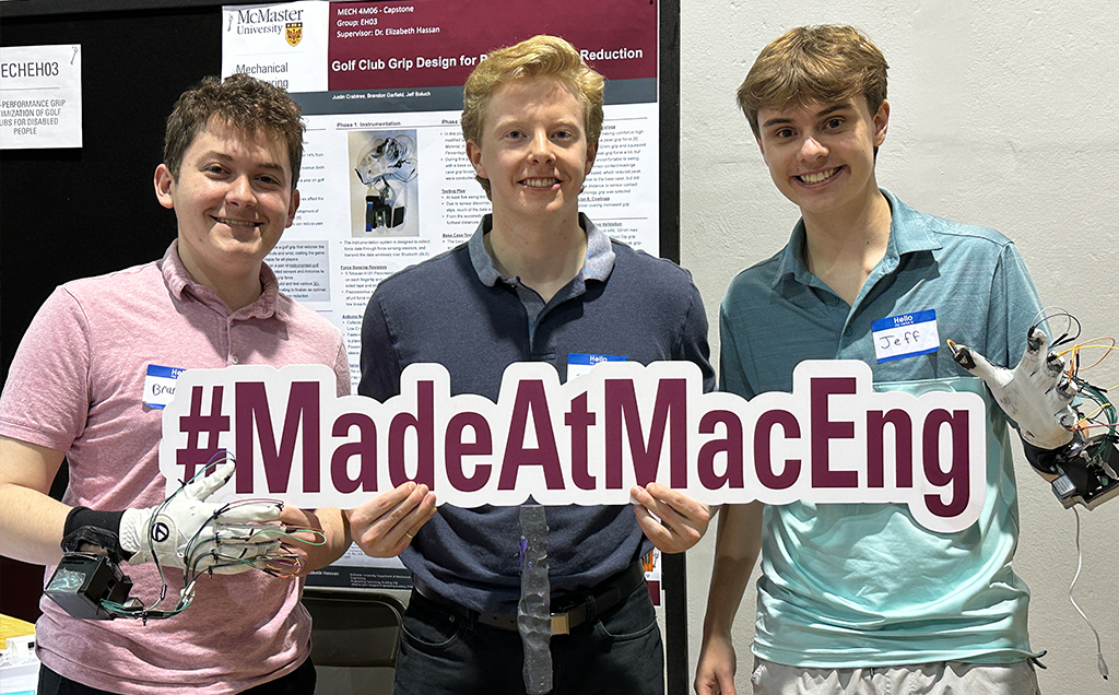 Three members pose holding a #MadeAtMacEng sign while wearing their golf gloves