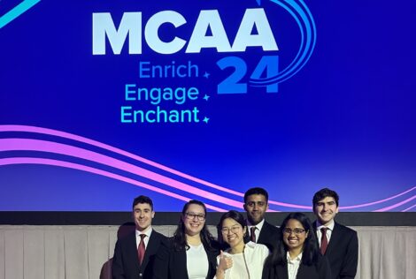 group of six students in business formal outfits posing in front of a powerpoint slide.