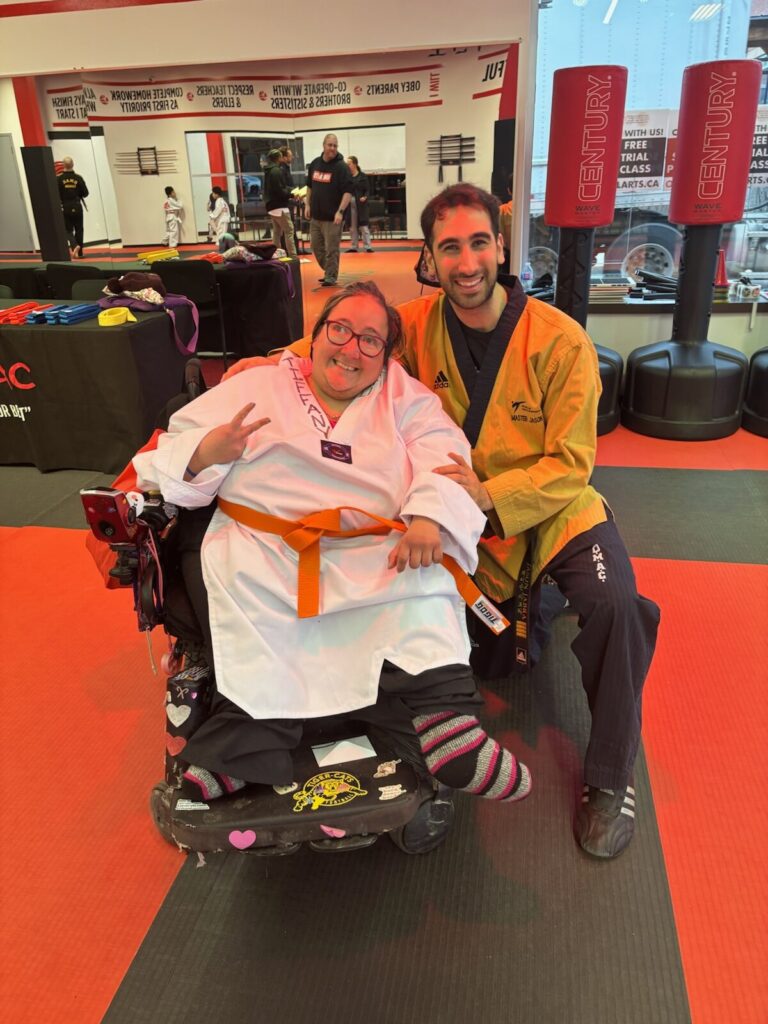 a woman in a wheelchair posing with a martial arts teacher at a martial arts studio.