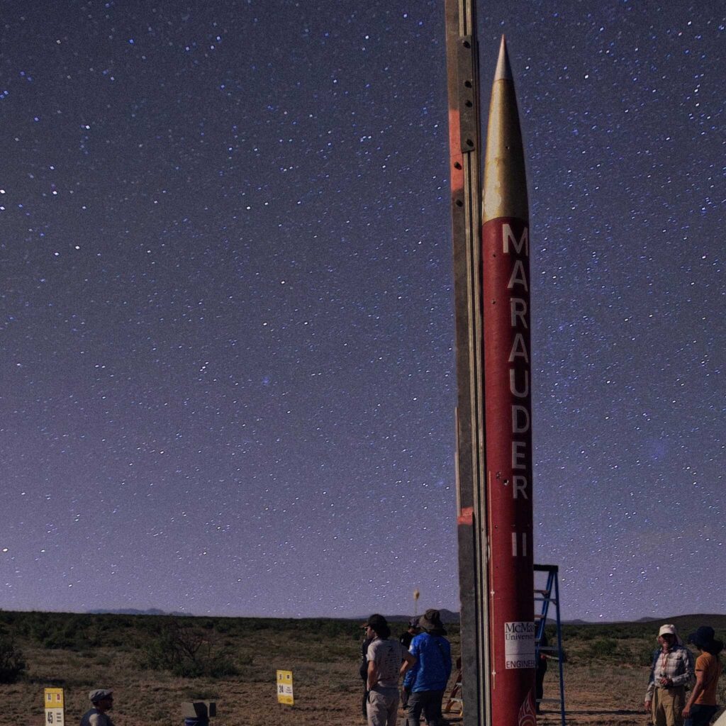 a rocket set upright against a starry night sky in the desert.