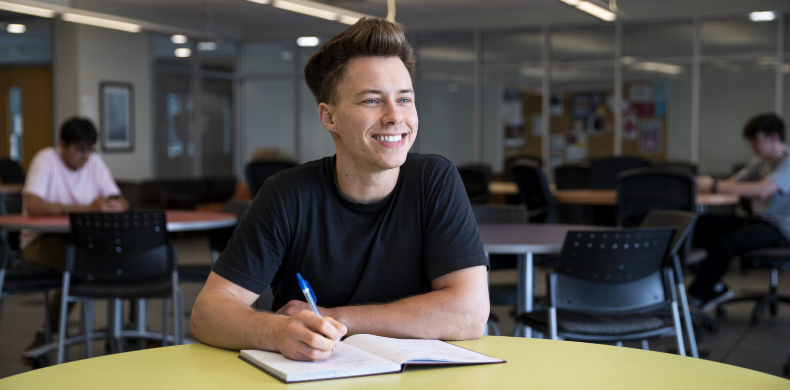 A student smiles while writing notes in a book