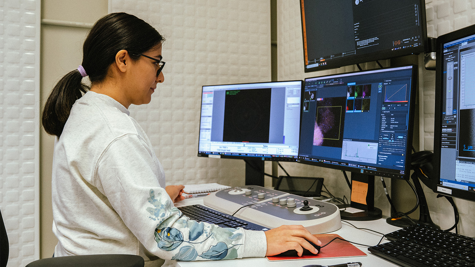 Zahra sits at a desk with four monitors