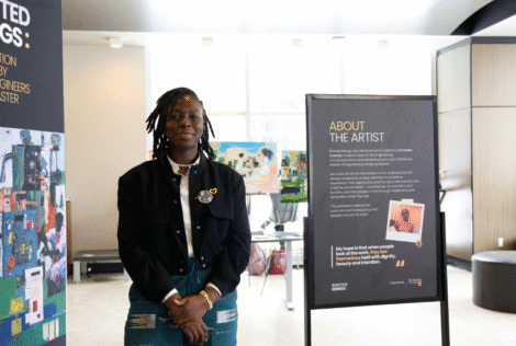 Artist Omoseke Fowode standing in front of the Rooted Beings exhibition in JHE Lobby on campus