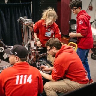 A team in red at a FIRST Robotics working on their robot.