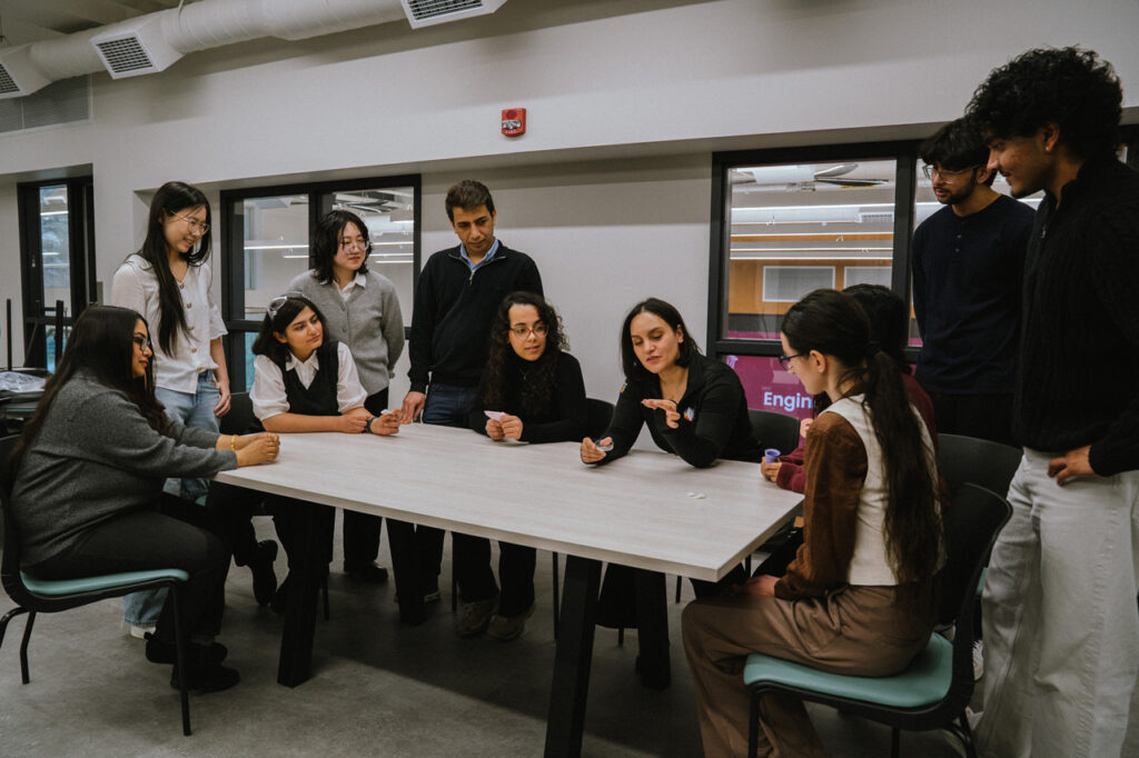 Zeinab is surrounded by grad students at a long table, she's holding up a tablet talking about it with everyone looking at her hands.
