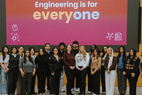 A group of women and men whose work at Mac Eng positively influences the lives of women pose together in front of a screen that reads engineering is for everyone