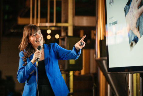 Shari van de Pol speaking in a microphone and pointing to a screen