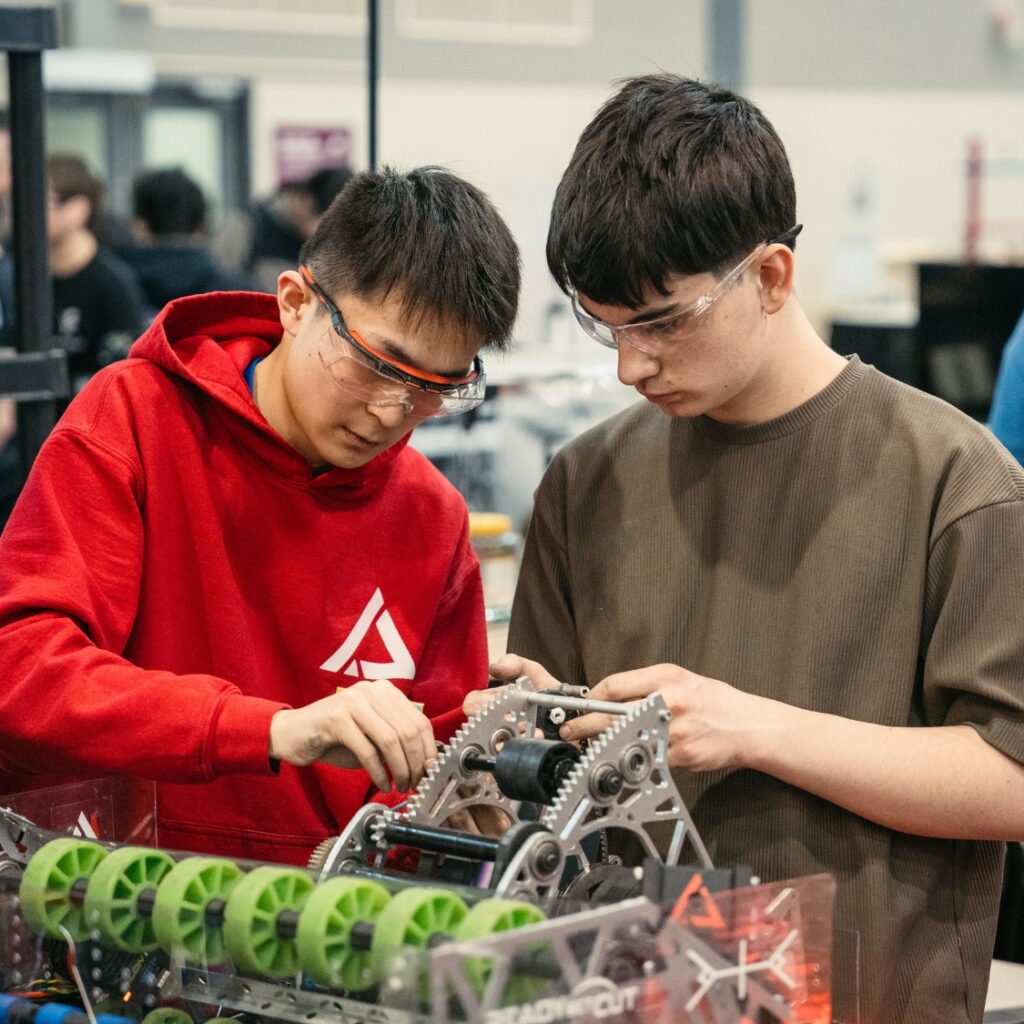 two students are working on a robot in the pit area