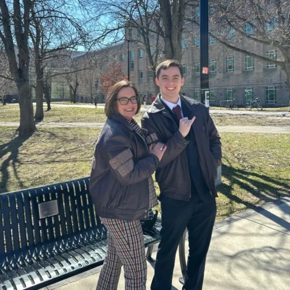 John and Nancy pose by a bench on campus with their pinkies up