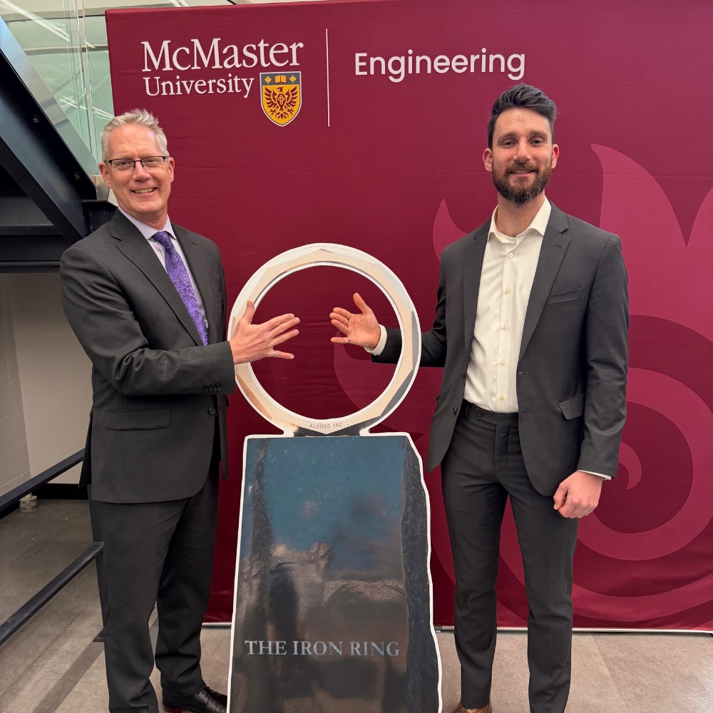 Stephen and Nathan pose at a iron ring cutout in front of an Engineering backdrop