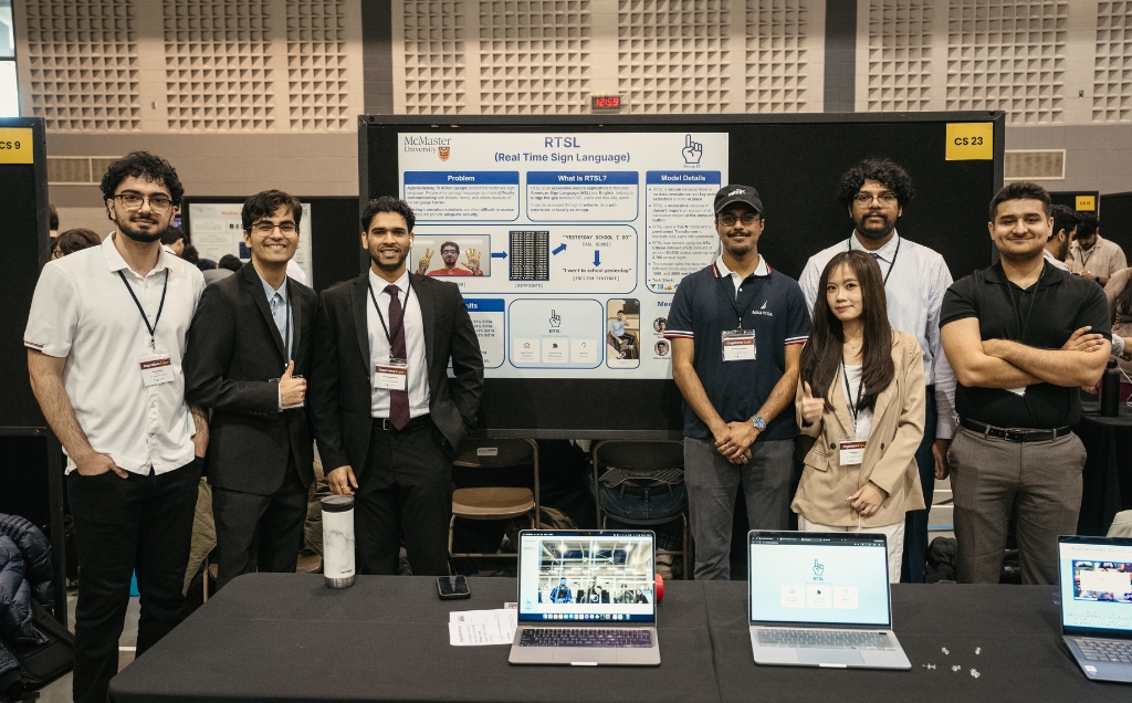 The Capstone team posing in their booth with their poster on a board and two laptops on their table