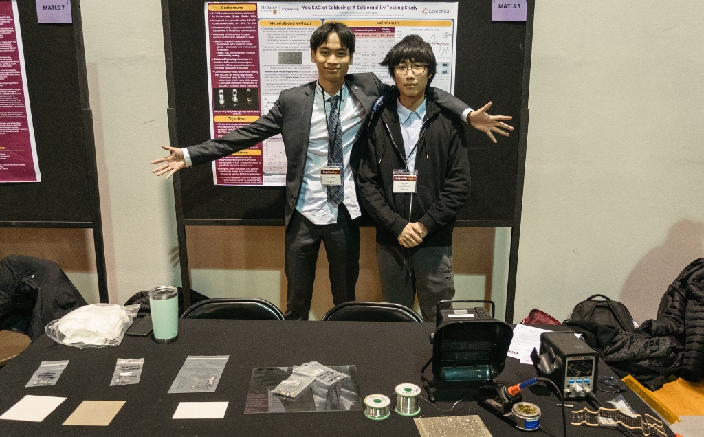 The two members pose at their table with their arms out to showcase the display of materials