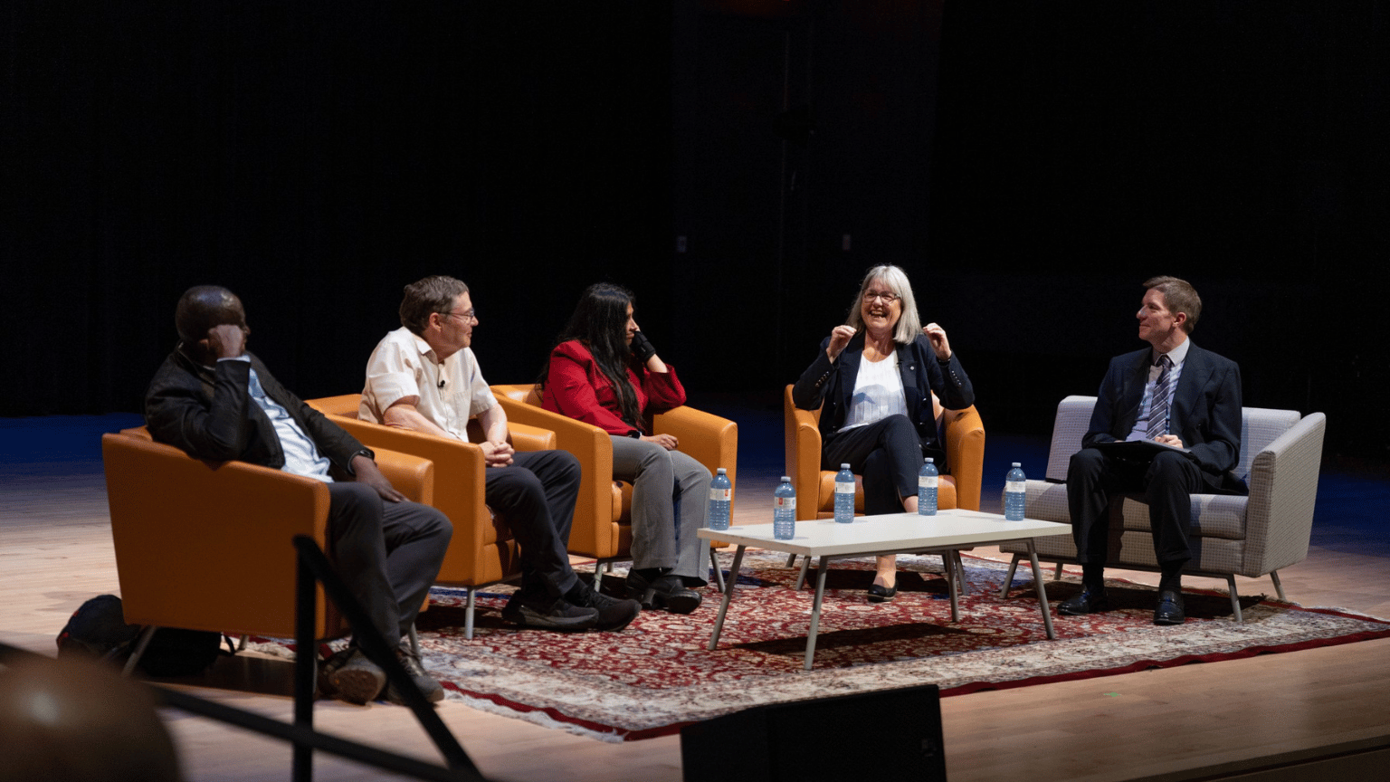 Martin Williams from the University of Guelph; Nobel Laureate and Stanford professor emeritus Carl Wieman; Wilfrid Laurier physicist Shohini Ghose, Nobel laureate and University of Waterloo professor Donna Strickland and panel moderator Rob Cockcroft sit in chairs on a stage during the panel.