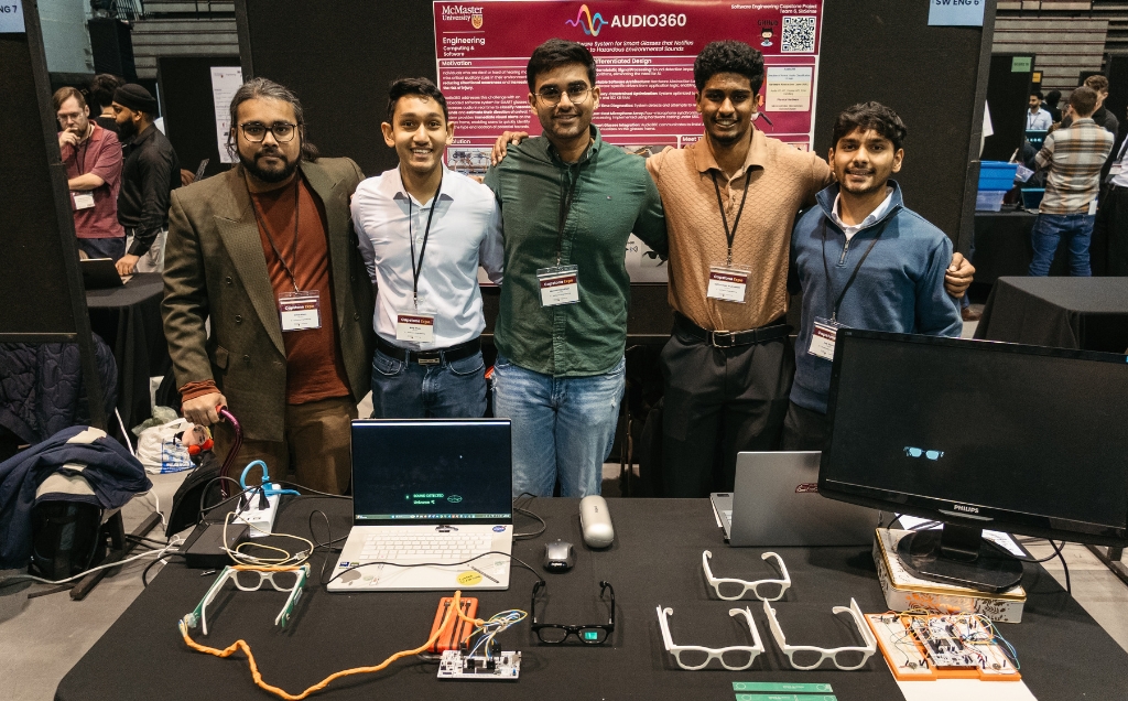 The SixSense team posing with their arms around each other and computers and eyewear displayed on their table