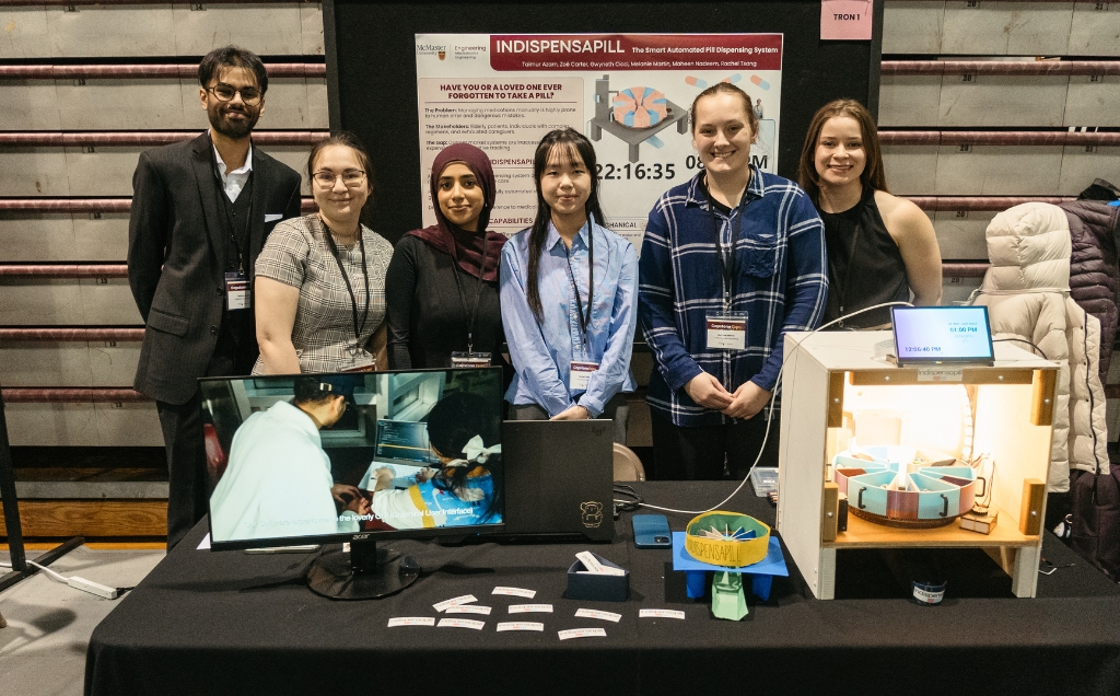The Tron group at their table with a monitor and their pill dispenser prototype