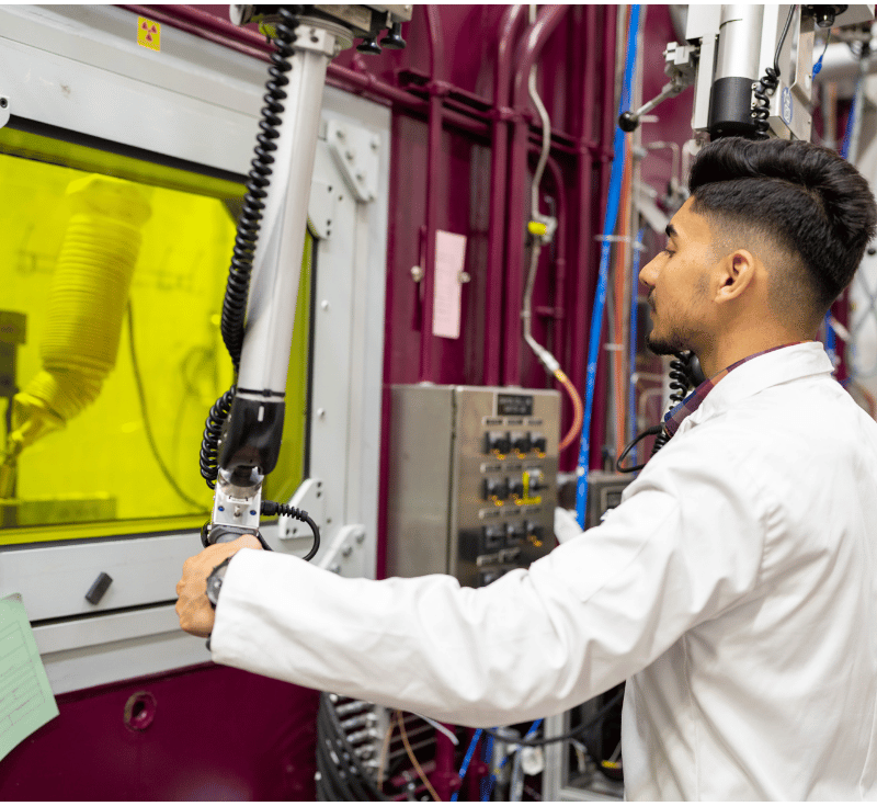 A person wearing a lab coat works in the hot cells.