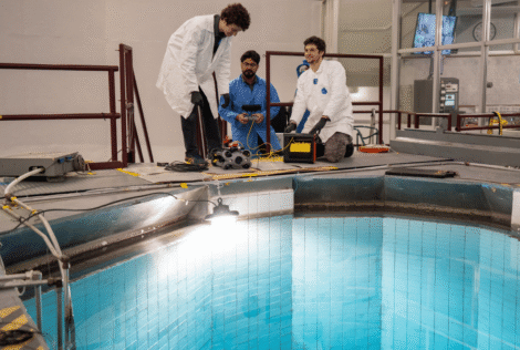 Three Engineering Physics students wearing lab coats prepare an underwater drone by the water of the McMaster Nuclear Reactor.