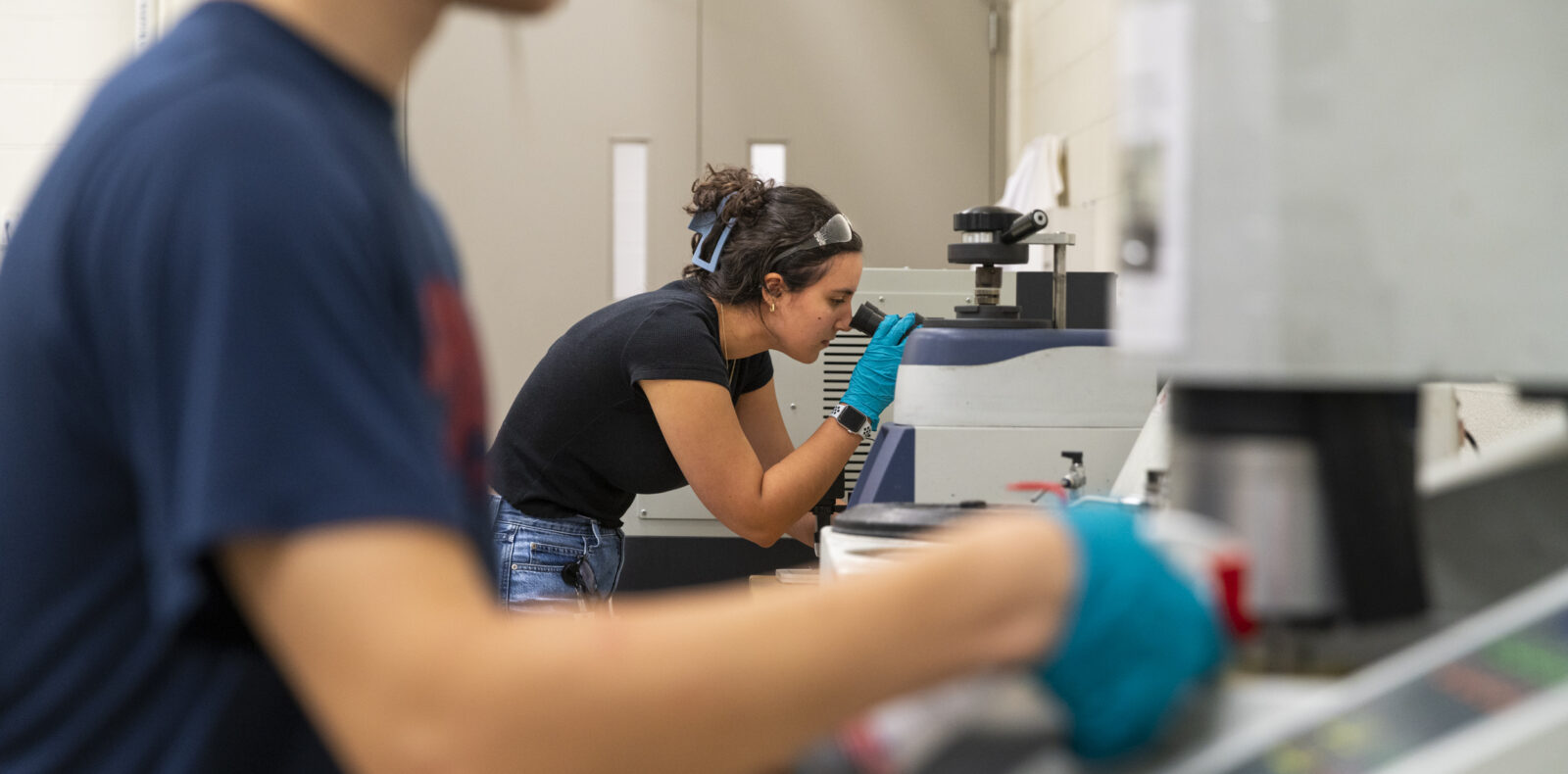 Two students working in a lab, one is in focus, one is not