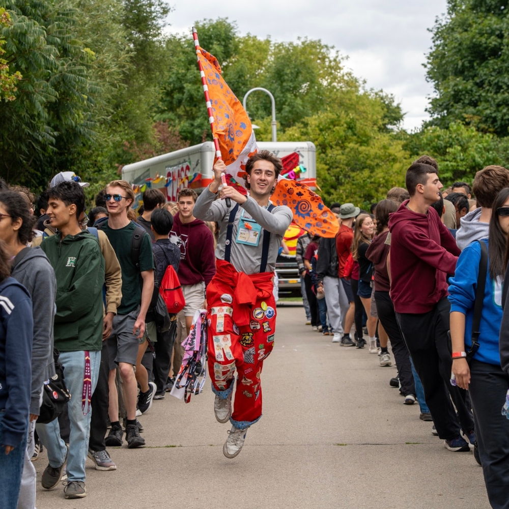 Nicholas running between two lines of people holding a MES flag and wearing a red suit