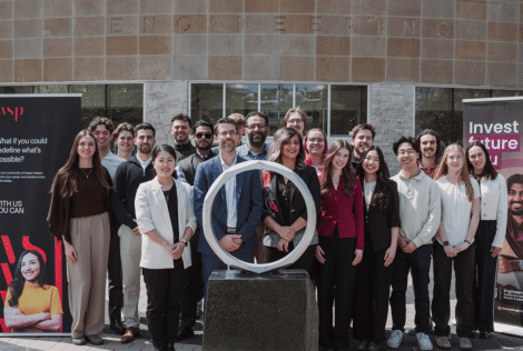 A group of people stand behind an iron ring statue outside of JHE with WSP and McMaster Engineering branded banners.