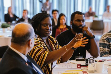 Opportunity Marketplace attendees sitting at a table, one is holding out her hands as she speaks asking a question to a speaker out of frame