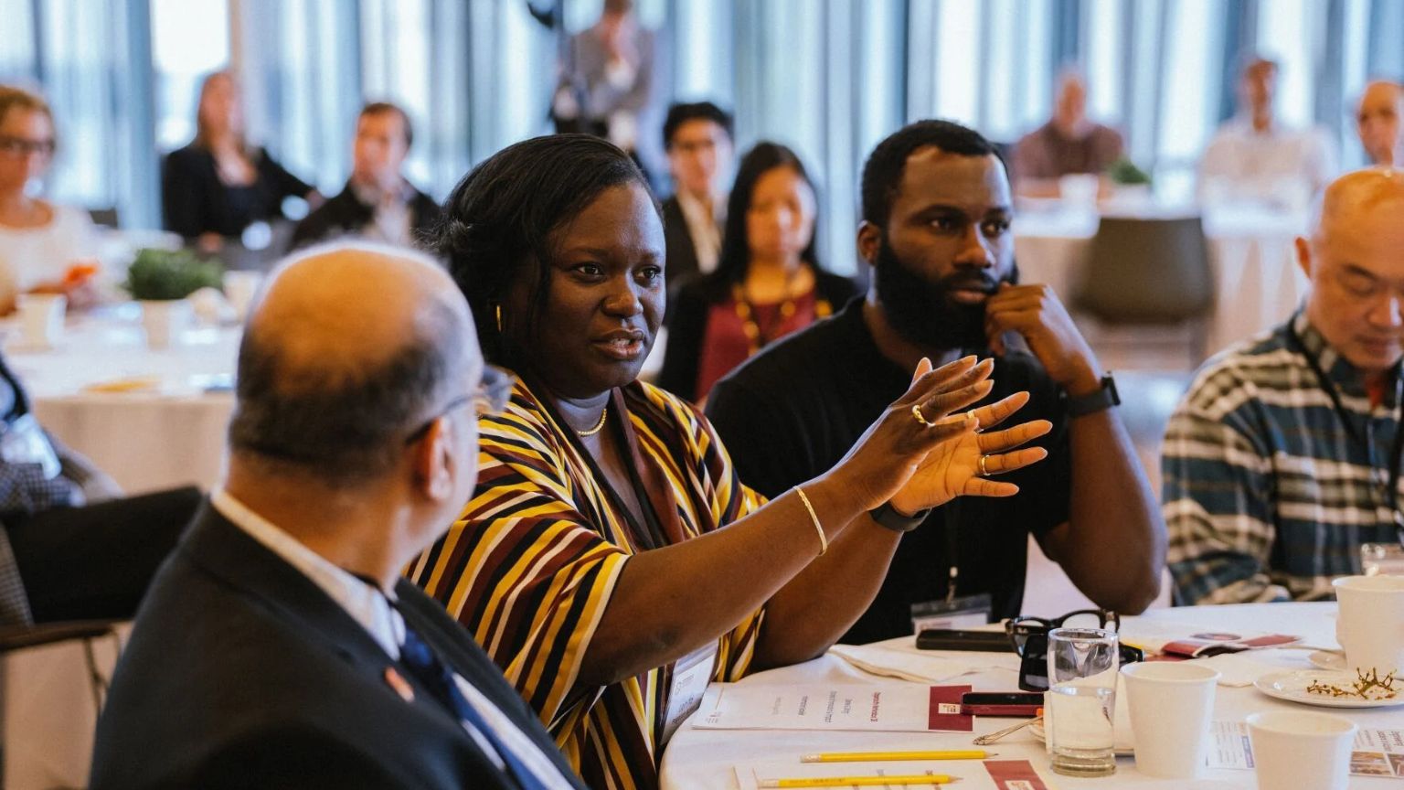 Opportunity Marketplace attendees sitting at a table, one is holding out her hands as she speaks asking a question to a speaker out of frame