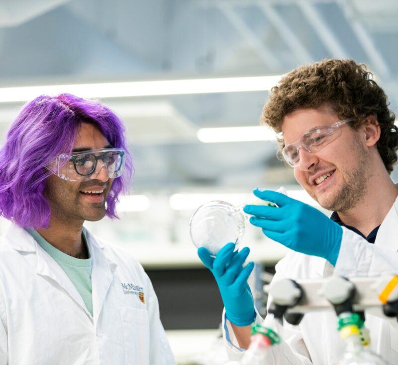 Two people wearing lab coats look at a flask.