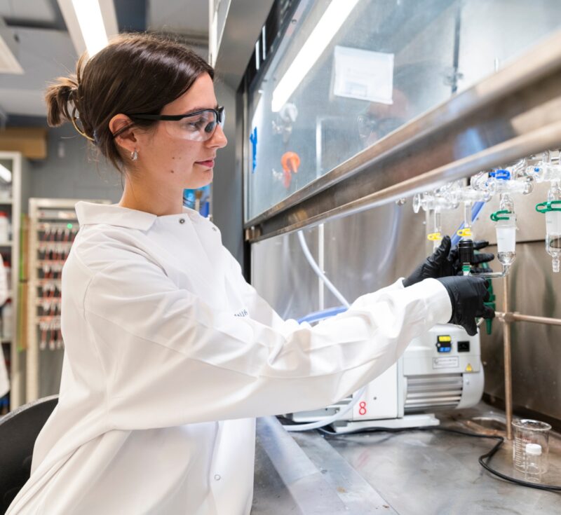 A student works with liquid under a laboratory fume hood.