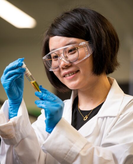 A person wearing safety glasses holds a test tube filled with liquid.