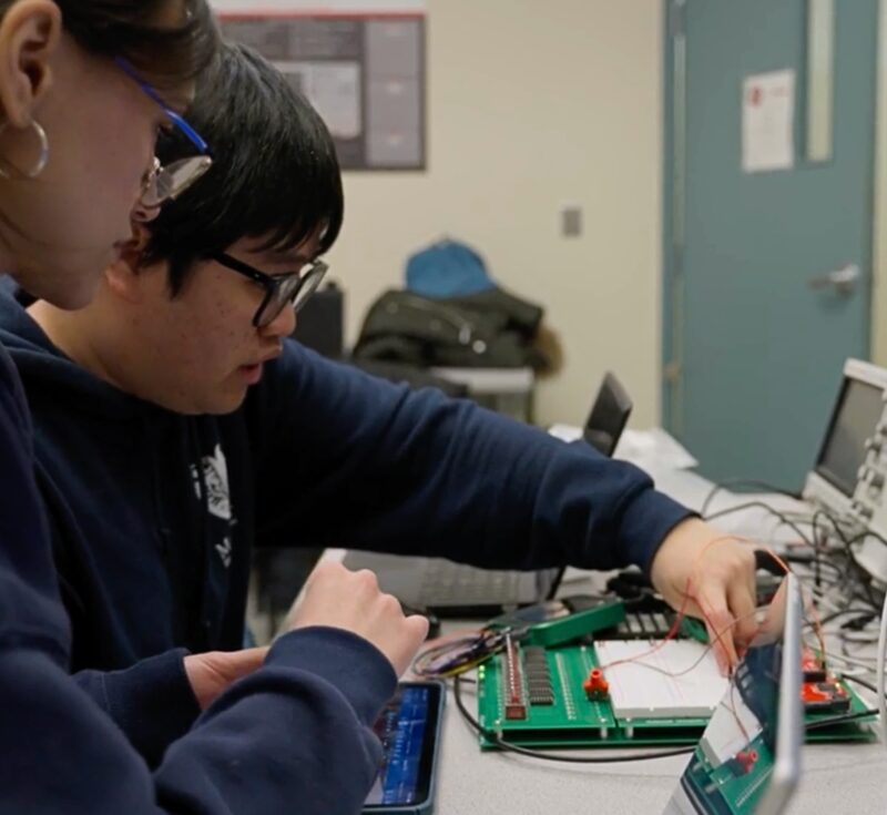 Two people work on a circuit board.