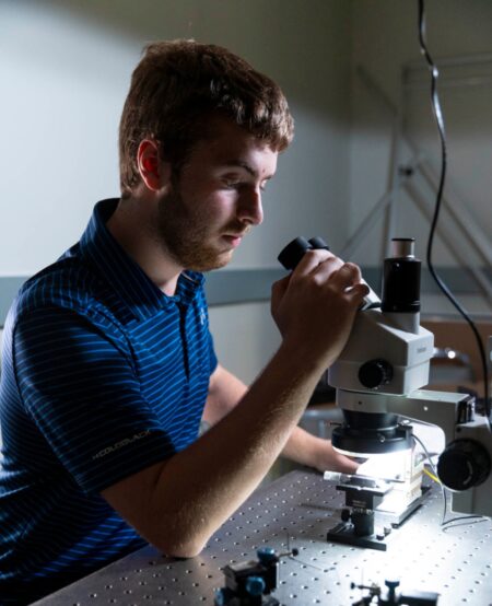 A student leans forward to peer into a microscope.