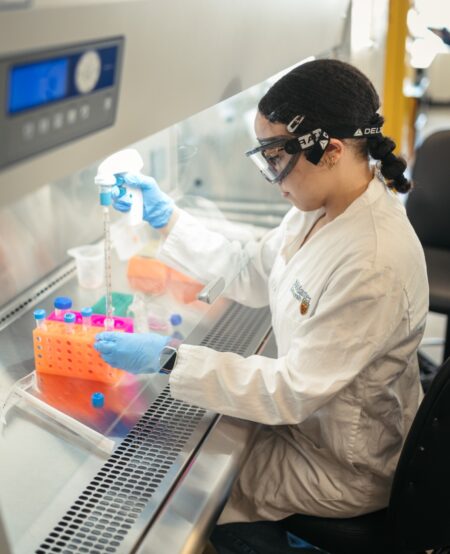A person wearing safety glasses conducts an experiment within a lab fume hood.
