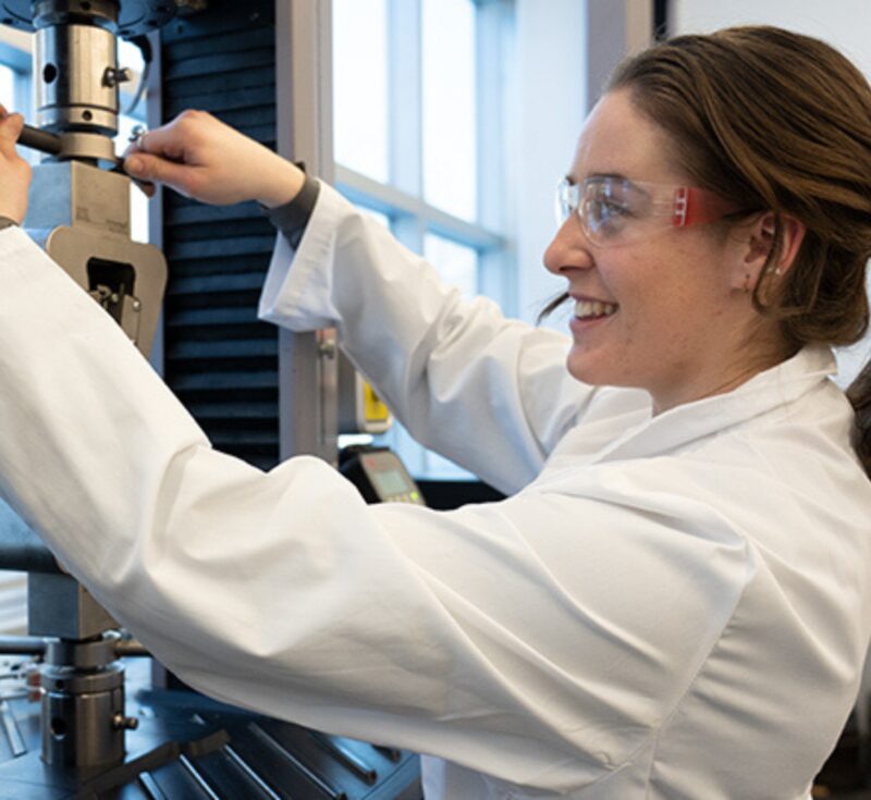 A person in a lab coat sets up machinery for a tensile test.
