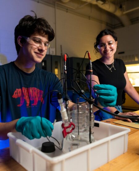 Two students wearing safety glasses perform a materials test.